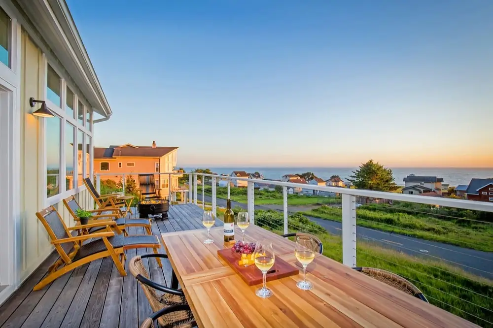 Ocean-view deck at Cottage by the Sea with an outdoor dining table, chairs, and sunset over the water.