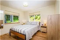 Guest bedroom with queen bed and windows overlooking greenery