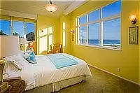 Bright yellow bedroom with a queen bed and large windows offering ocean views.