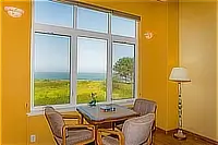 Small sitting area with a table and cushioned chairs beside tall windows offering ocean views.