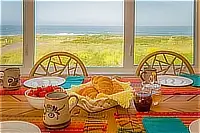 Breakfast setting with croissants, strawberries, and coffee on a wooden dining table overlooking the ocean.