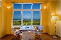 Cozy sitting area with three upholstered chairs and a small table positioned in front of an ocean-view window.