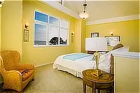 Yellow bedroom with a queen bed, wicker armchair, and a large window overlooking the ocean.