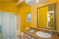 Yellow bathroom with a bathtub and shower, granite vanity, and large framed mirror.