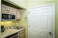 Compact kitchenette with microwave, sink, countertop, and light-colored cabinets.