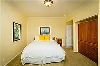 Bedroom with a queen bed, yellow accent pillows, wooden dresser, and neutral-colored walls.