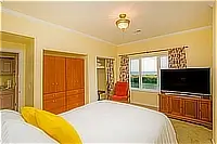 Bedroom with a queen bed, television, wooden wardrobe, and window overlooking the coast.
