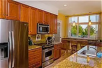 Kitchen with wooden cabinets, stainless steel appliances, granite countertops, and a window overlooking the coast.