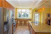 Bright kitchen with granite island, stainless steel refrigerator, wooden cabinets, and breakfast seating by the windows.